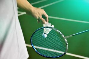 Badminton player holds racket and white cream shuttlecock in front of the net before serving it to another side of the court. photo