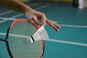 Badminton player holds racket and white cream shuttlecock in front of the net before serving it to another side of the court. photo