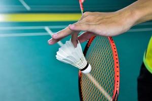 Badminton player holds racket and white cream shuttlecock in front of the net before serving it to another side of the court. photo