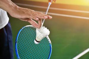 Badminton player holds racket and white cream shuttlecock in front of the net before serving it to another side of the court. photo