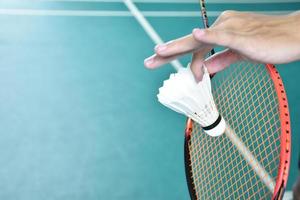 Badminton player holds racket and white cream shuttlecock in front of the net before serving it to another side of the court. photo