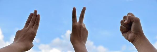 Hands of human in fist, three and two fingers show on cloudy and bluesky background. Soft and selective focus on fingers. photo