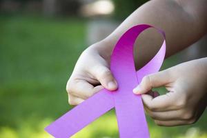 Pink paper ribbon holding in hands of female teenager to show and to call out all people around the world to support and to attend the breast cancer campaign of woman, soft and selective focus. photo