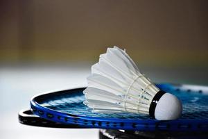 volante de bádminton blanco crema y raqueta con sombreado de luz de neón en el suelo verde en la cancha de bádminton cubierta, fondo de bádminton borroso, espacio para copiar. foto