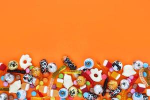 Orange background with copy space, halloween assorted candies at bottom - traditional eyeballs chocolates, jelly worms, ghosts. Happy Halloween holiday sale and trick-or-treat concept. photo