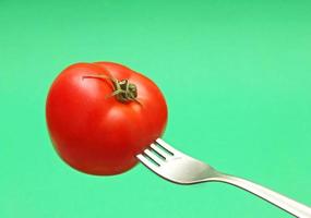 fresh tomato on fork with green background photo