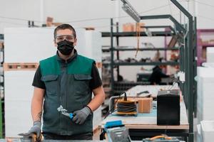 Heavy Industry Engineering Factory Interior with Industrial Worker Using Angle Grinder and Cutting a Metal Tube.He Wears a Mask on His Face Because of the Coronavirus Pandemic photo