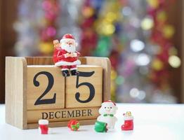 Santa sitting on wooden block date dated 25 December with snowman and gifts waiting for fun festival Christmas and Happy New Year to make greeting card. photo