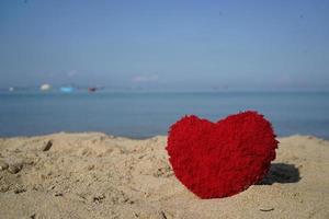 forma de corazón rojo en la playa de arena en la costa para crear una tarjeta dulce y encantadora y un póster de pareja. foto