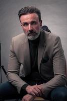 Portrait of adult businessman wearing trendy suit and sitting in modern studio on stylish chair against the black background photo