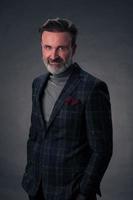 Portrait of a stylish elegant senior businessman with a beard and casual business clothes in photo studio isolated on dark background gesturing with hands