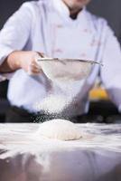 chef sprinkling flour over fresh pizza dough photo