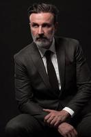 Portrait of a stylish elegant senior businessman with a beard and casual business clothes in photo studio isolated on dark background gesturing with hands