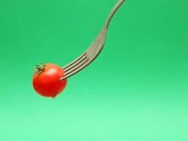 fresh tomato on fork with green background photo