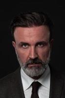 retrato de un elegante hombre de negocios de alto nivel con barba y ropa informal de negocios en un estudio fotográfico aislado en un fondo oscuro gesticulando con las manos foto