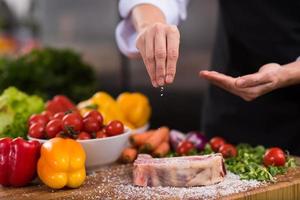 Chef putting salt on juicy slice of raw steak photo