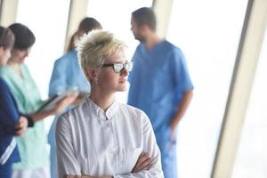 female doctor with glasses and blonde hairstyle standing in front of team photo