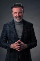 Portrait of a stylish elegant senior businessman with a beard and casual business clothes in photo studio isolated on dark background gesturing with hands