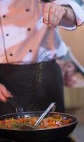 chef putting spices on vegetables in wok photo