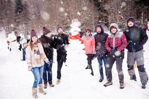 group portait of young people posing with snowman photo