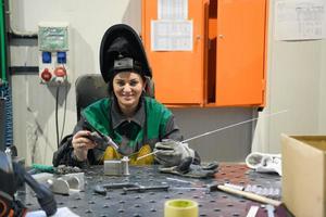 una mujer empleada en una fábrica moderna para la producción y procesamiento de metales en un uniforme de trabajo suelda materiales metálicos foto