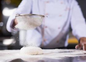 chef sprinkling flour over fresh pizza dough photo