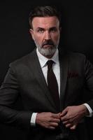 Portrait of a stylish elegant senior businessman with a beard and casual business clothes in photo studio adjusting suit