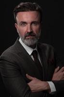 Portrait of a stylish elegant senior businessman with a beard and casual business clothes in photo studio isolated on dark background gesturing with hands