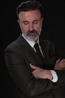 Portrait of a stylish elegant senior businessman with a beard and casual business clothes in photo studio isolated on dark background gesturing with hands