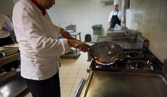 chef en la cocina del hotel prepara comida con fuego foto