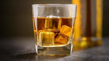 A glass of Whiskey with ice cube on wooden table photo