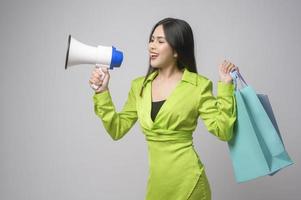 Beautiful woman holding megaphone and shopping bag over white background studio, shopping and finance concept. photo