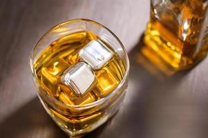 A glass of Whiskey with ice cube on wooden table photo