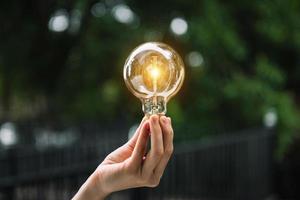 Hand holding light bulb with green background. idea solar energy in nature concept