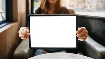 Mockup image of a beautiful woman holding and showing a tablet and smartphone with blank white screen while sitting on sofa at cafe photo