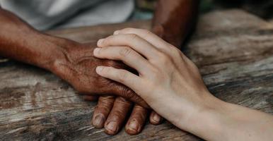 Hands of the old man and a woman hand on the wood table in sun light photo