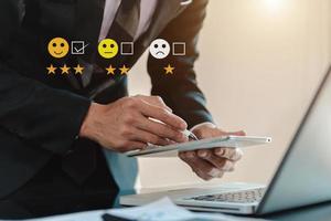 concepto de evaluación del servicio al cliente. mujer de negocios presionando el espectáculo de emoticonos de sonrisa en la pantalla virtual en la tableta y el teléfono inteligente en la oficina foto