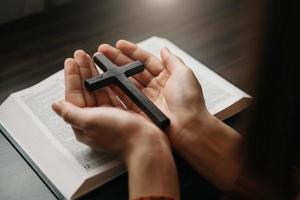 Woman sitting and studying the scriptures.The  wooden cross in the hands. Christian education concepts The Holy Scriptures open and pray to God. photo