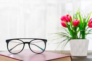 Reading glasses put on hardcover book beside the window photo