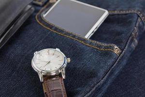 Wrist watch and smartphone on denim jeans photo