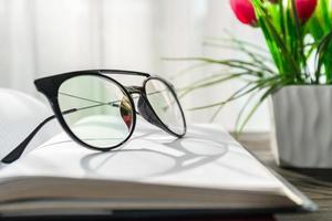 Reading glasses put on open book beside the window photo