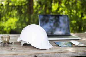 White helmet and computer at cafe with sunlight background, engineer view sitting construction planning photo