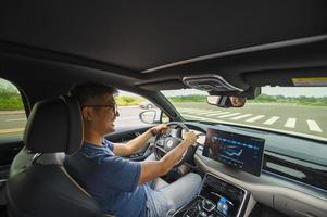 An Asian man drives from town to go on a summer vacation. Happy Asian man in casual wear and beautiful new driving glasses. photo