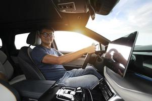 An Asian man drives from town to go on a summer vacation. Happy Asian man in casual wear and beautiful new driving glasses. photo