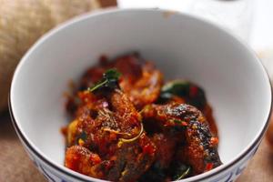 Spicy Stir Fried Catfish served in a Thai style patterned bowl on a white table. photo