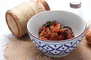 Spicy Stir Fried Catfish served in a Thai style patterned bowl on a white table. photo