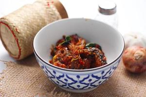 Spicy Stir Fried Catfish served in a Thai style patterned bowl on a white table. photo