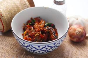 Spicy Stir Fried Catfish served in a Thai style patterned bowl on a white table. photo