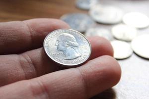 mano recogiendo un cuarto de moneda en moneda americana esparcida en el suelo de madera foto