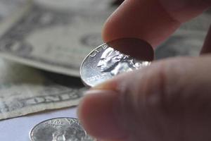 la mano del hombre recogiendo un cuarto de moneda de un montón de billetes y monedas. foto